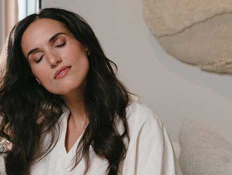 Frau mit dunklen Haaren und geschlossenen Augen fährt sich mit der Hand durch das lange Haar