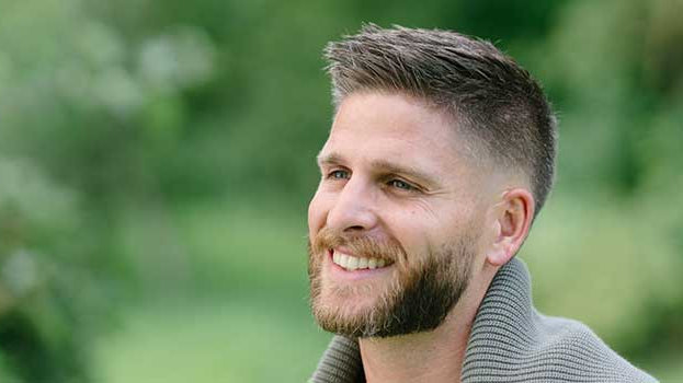 Lächelnder, schöner Mann mit vollem Haar in der Natur