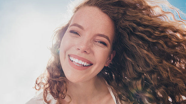Frau mit lockigen, schuppenfreien Haaren lächelt in die Kamera