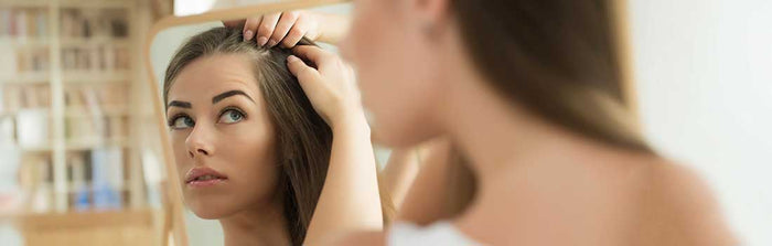 Frau mit Haarausfall schaut besorgt in den Spiegel