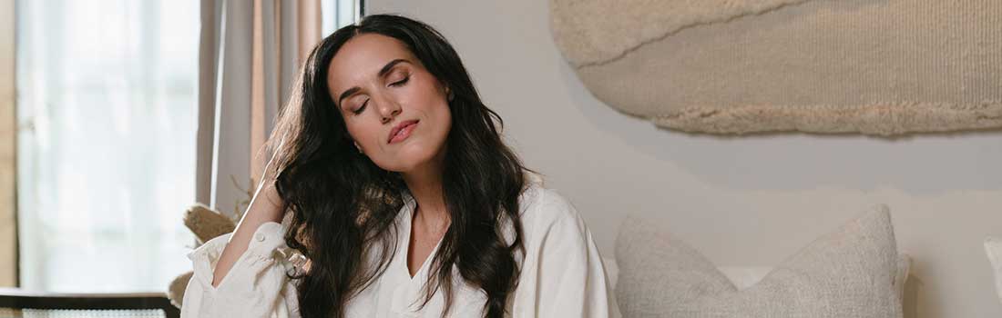 Frau mit dunklen Haaren und geschlossenen Augen fährt sich mit der Hand durch das lange Haar