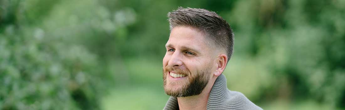 Lächelnder, schöner Mann mit vollem Haar in der Natur