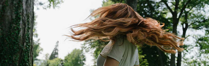 Frau in der Natur dreht ihren Kopf, dabei fliegen die langen roten Haare