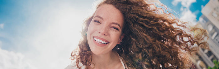 Frau mit lockigen, schuppenfreien Haaren lächelt in die Kamera